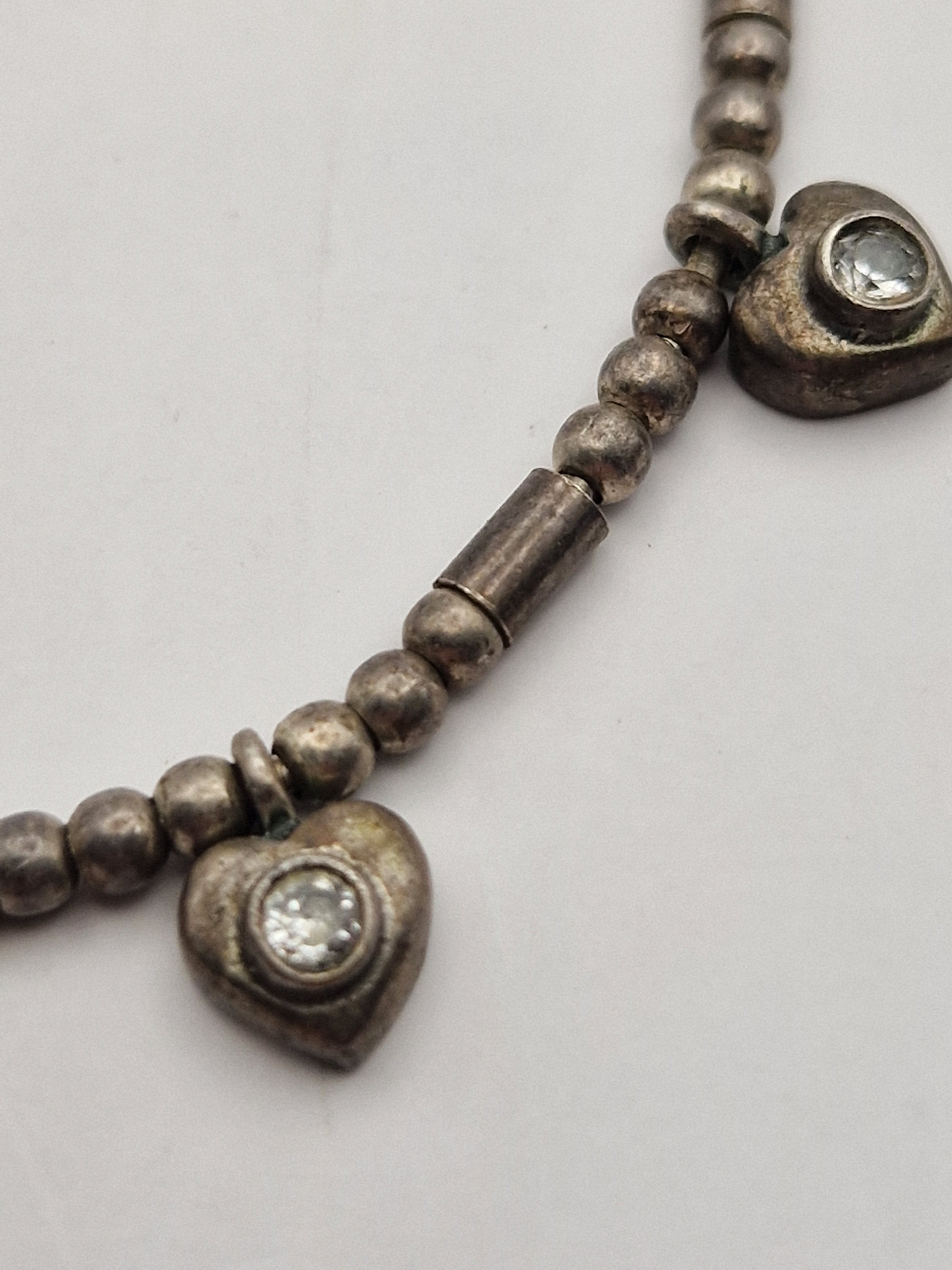 Detalj av sølvkjede med hjerteanheng og klare steiner